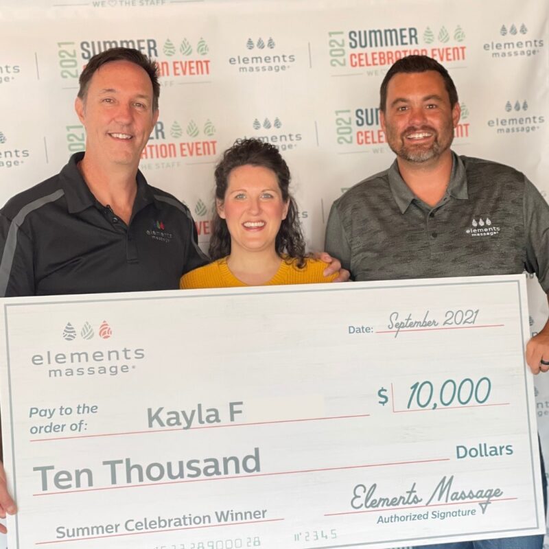 Kayla F along with 2 other men holding a large check fpor the amount of ten thousand dollars from elements massage