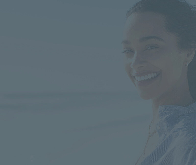 woman looking over left shoulder at camera with beach in the background.